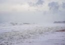 A stormy beach scene with crashing waves and mist, creating a moody atmosphere.