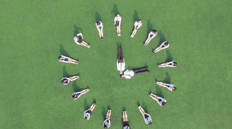 Aerial view of students forming a clock shape on a green field, symbolizing teamwork and time management.