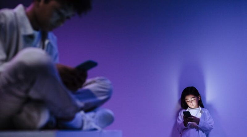 Two kids focusing on their smartphones in a dimly lit studio environment.