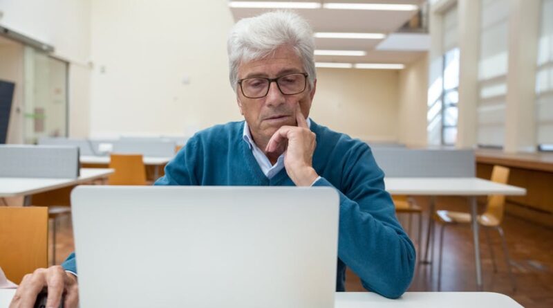 Mature man focused on laptop work in a contemporary library setting.
