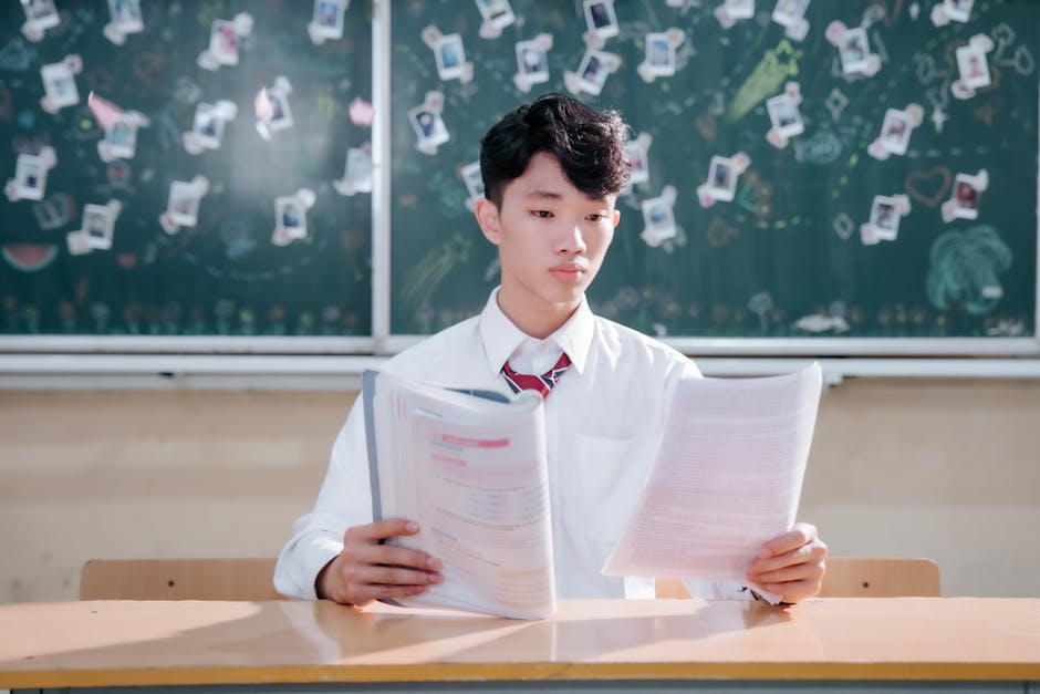 Focused student reading papers at desk in a classroom.