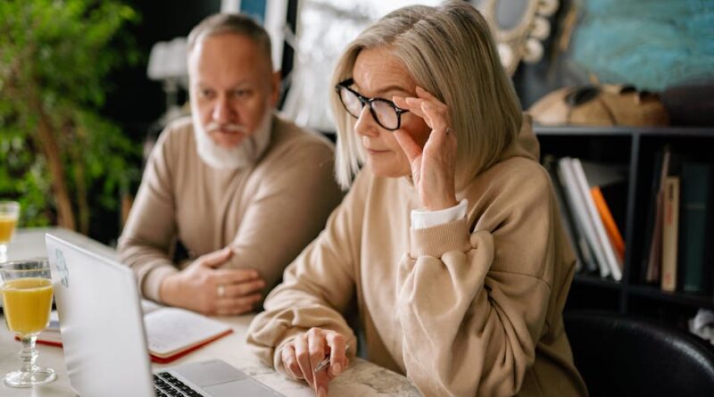 Elderly couple looking at laptop screen indoors, focused and engaged in a task.