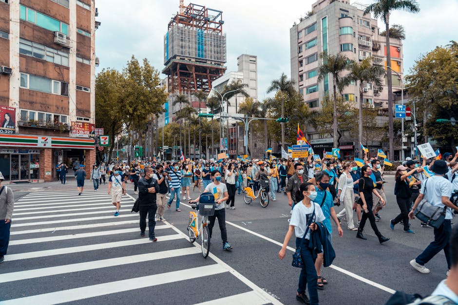 A large group of people in a city protest, wearing masks and carrying banners.