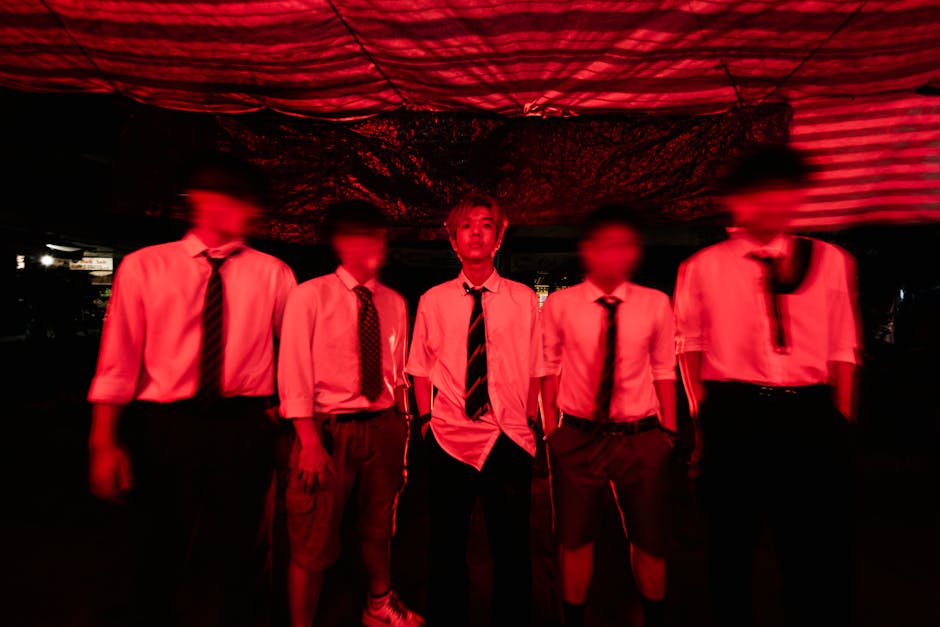 Blurred group of young men in white shirts and ties under red lighting.