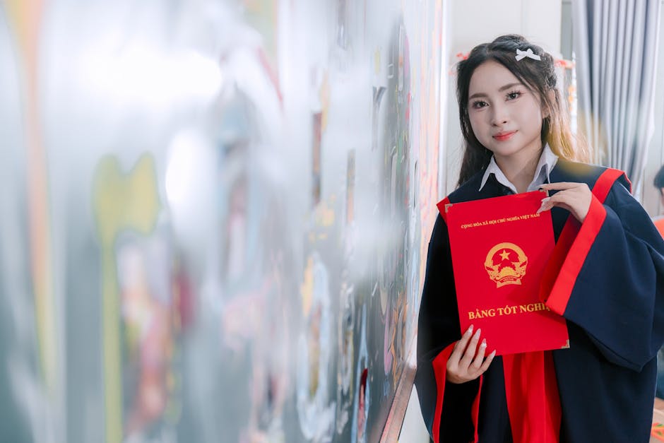 A young woman in a graduation gown holding a diploma with a blurred artistic background indoors.
