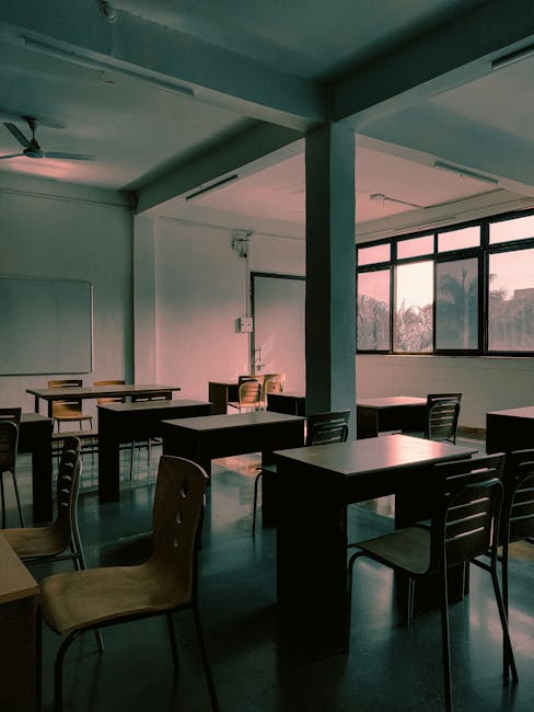 Empty classroom with wooden desks and chairs, India, natural sunlight pouring through windows.