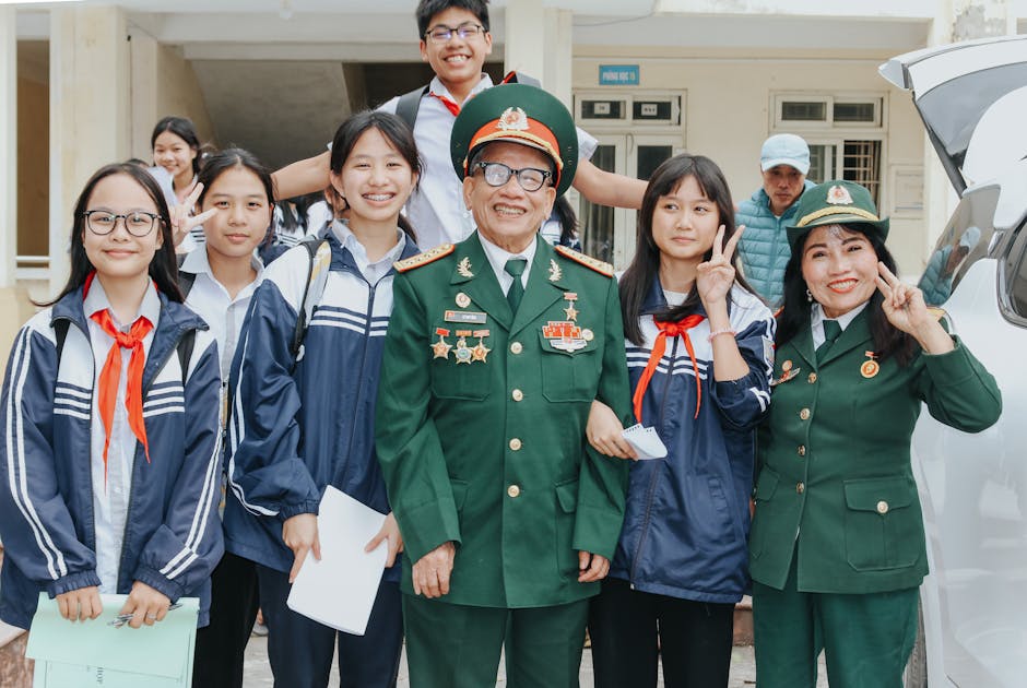A group of smiling students posing with military veterans during a school event outdoors.