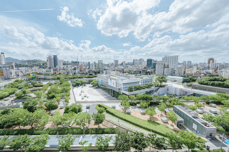 Aerial shot of a modern city with green parks, cloudy sky, and high-rise buildings.