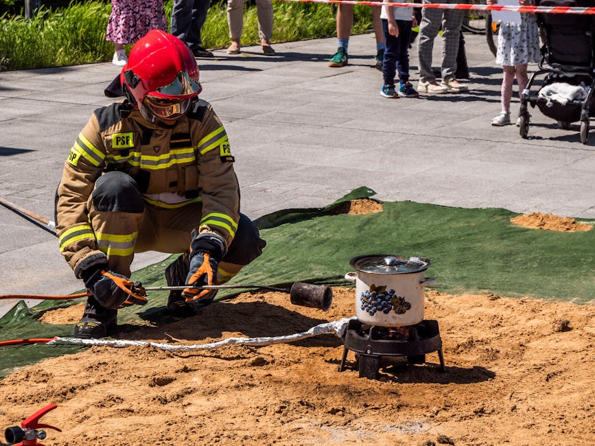 Firefighter in protective gear demonstrating fire safety during an outdoor drill with people watching.