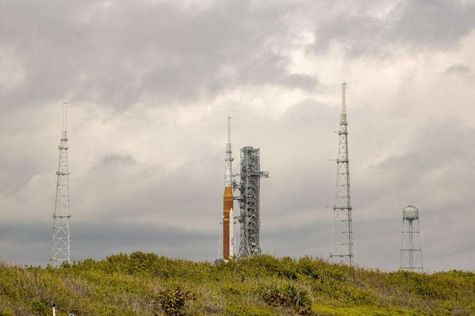 NASA rocket on launch pad surrounded by antennas against a cloudy sky.