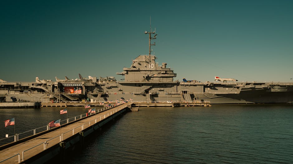View of USS Yorktown aircraft carrier docked at harbor with walkway and flags.
