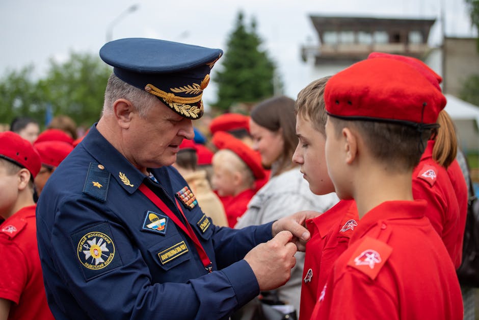 A Russian officer in uniform pinning a badge on a young recruit during an outdoor military ceremony.