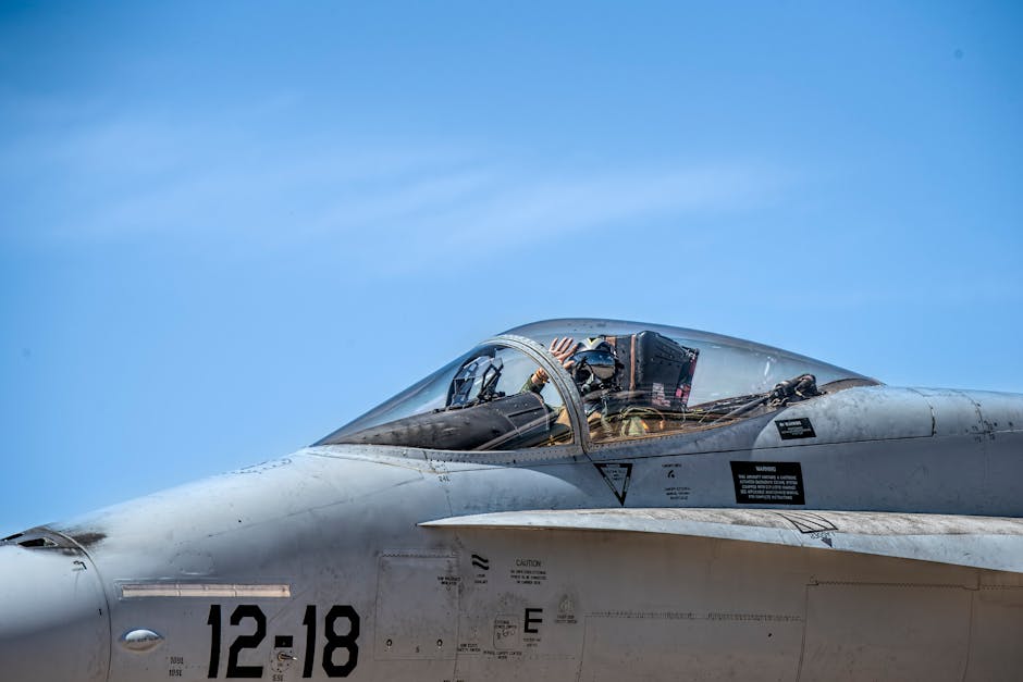 Close-up of a fighter jet pilot in the cockpit under a clear blue sky, showcasing aviation details.