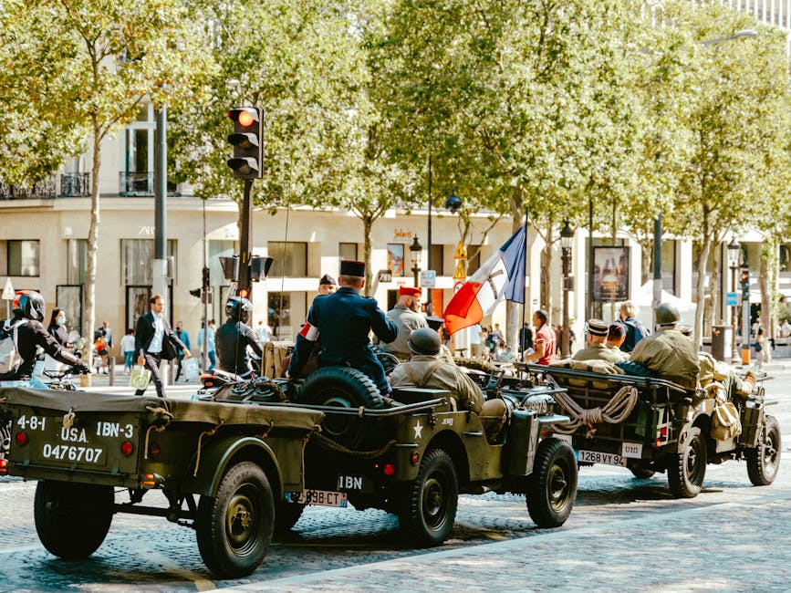 Vintage military jeeps in a parade, featuring soldiers and French flags in an urban setting.
